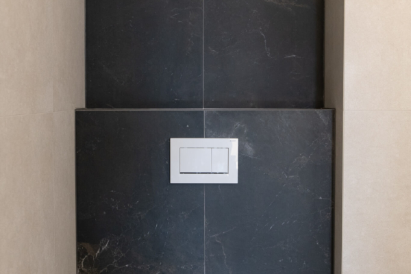Toilettes encastrée dans une niche de carrelage noir autour d'un carrelage beige. Salle de bain après rénovation à Pully