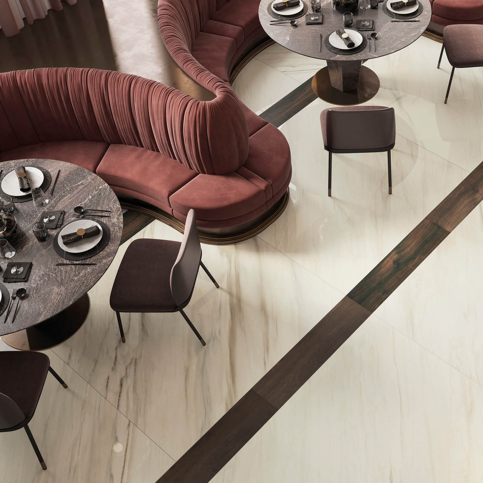 Marmi Maximum Palissandro White 4 Restaurant avec canapé circulaire en velours rouge, positionné autour de tables rondes en marbre. Le sol est recouvert de grands carreaux carrelage imitation marbre Marmi Maximum Palissandro avec des bandes de bois foncé créant un contraste dynamique. L'éclairage doux et l'atmosphère accueillante dominent la scène.