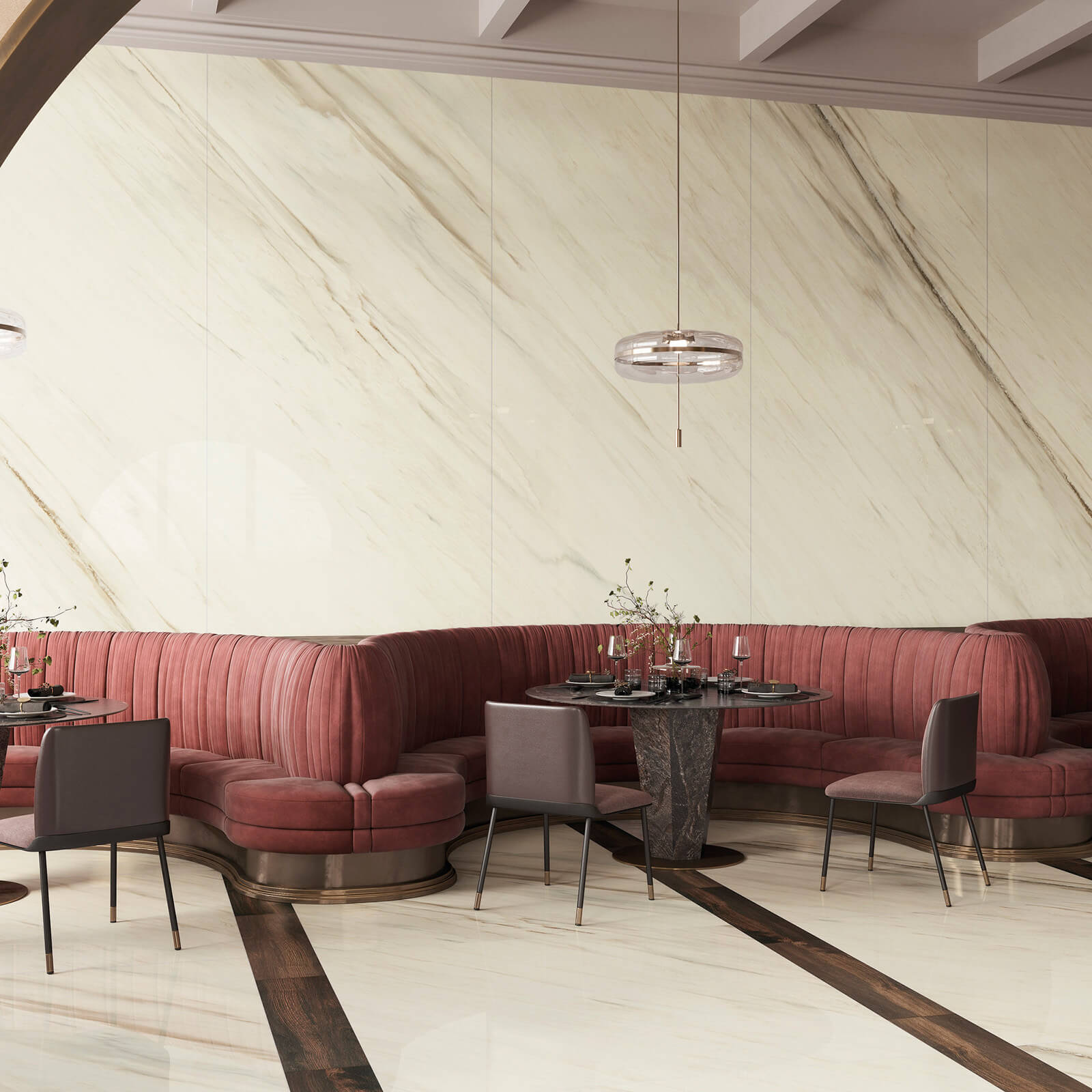 Marmi Maximum Palissandro White 3 Vue d’un coin de café avec une banquette rouge continuant le long du mur courbé. Le mur derrière est recouvert de grandes dalles de carrelage imitation marbre Marmi Maximum Palissandro qui ajoutent une texture riche à l'espace. L'éclairage suspendu moderne et des éléments décoratifs discrets complètent l'ambiance raffinée.