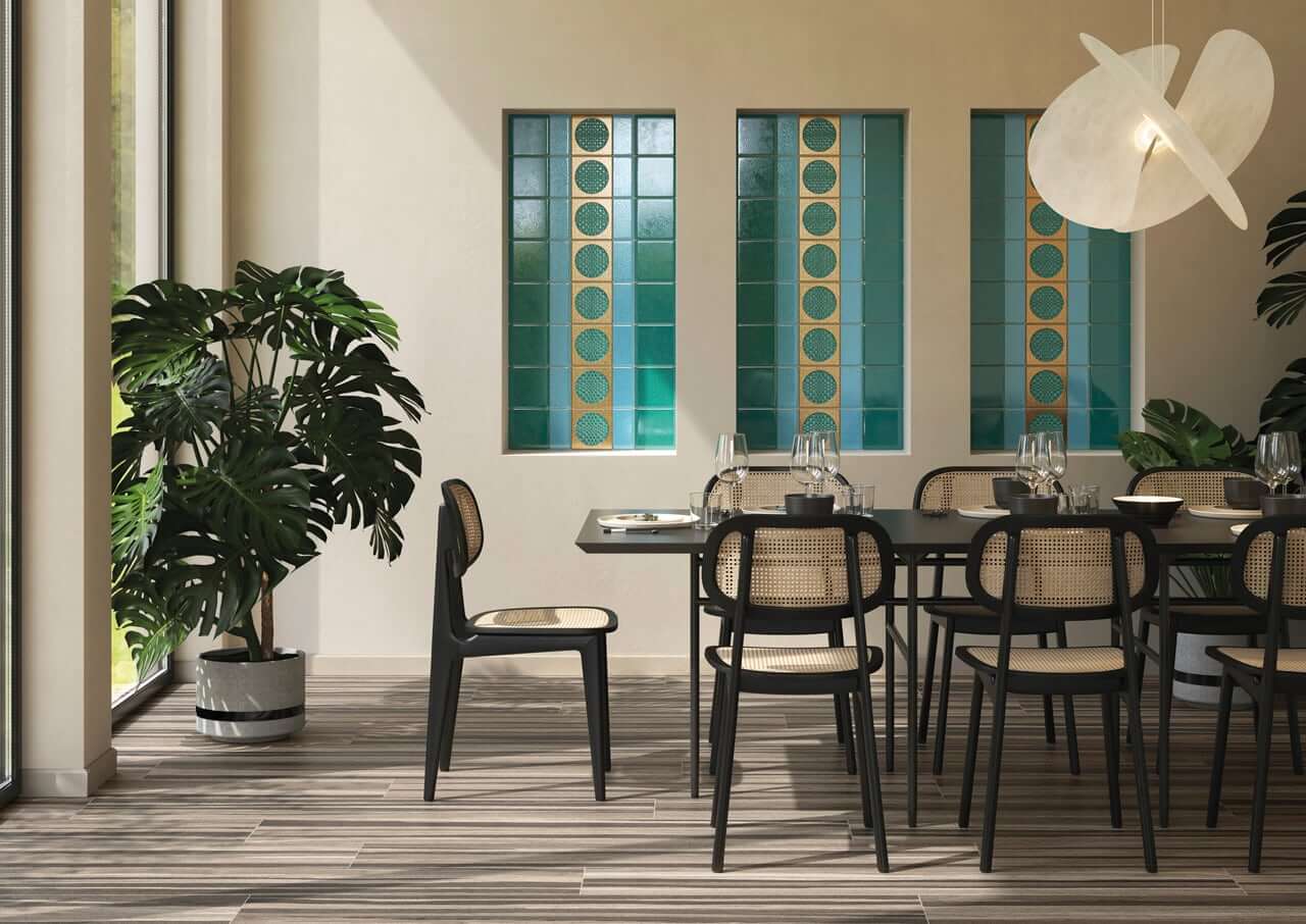 Bottega d'Arte Citta Di Faenza Oro 3 Salle à manger tropicale avec grands carreaux décoratifs verts et dorés sur le mur, meubles en noir mat et sièges en rotin, grande plante verte, collection bottega d'arte città di faenza oro.