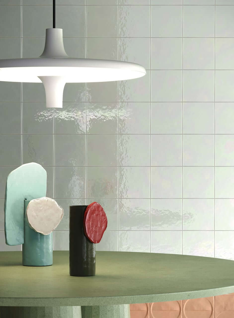 Bottega d'Arte TerreLustrate 2 gros plan d'une table de bar avec des carreaux de faïence Bottega d'Arte TerreLustrate vert pâle et une lampe suspendue blanche, vases en céramique de différentes formes et couleurs sur la table