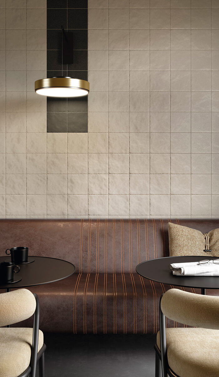 Bottega d'Arte TerreCotte 3 Intérieur de café chic avec banquette en cuir brun et table ronde noire, éclairage doré, mur en carreaux de céramique gris et noirs, collection bottega d'arte terrecotte
